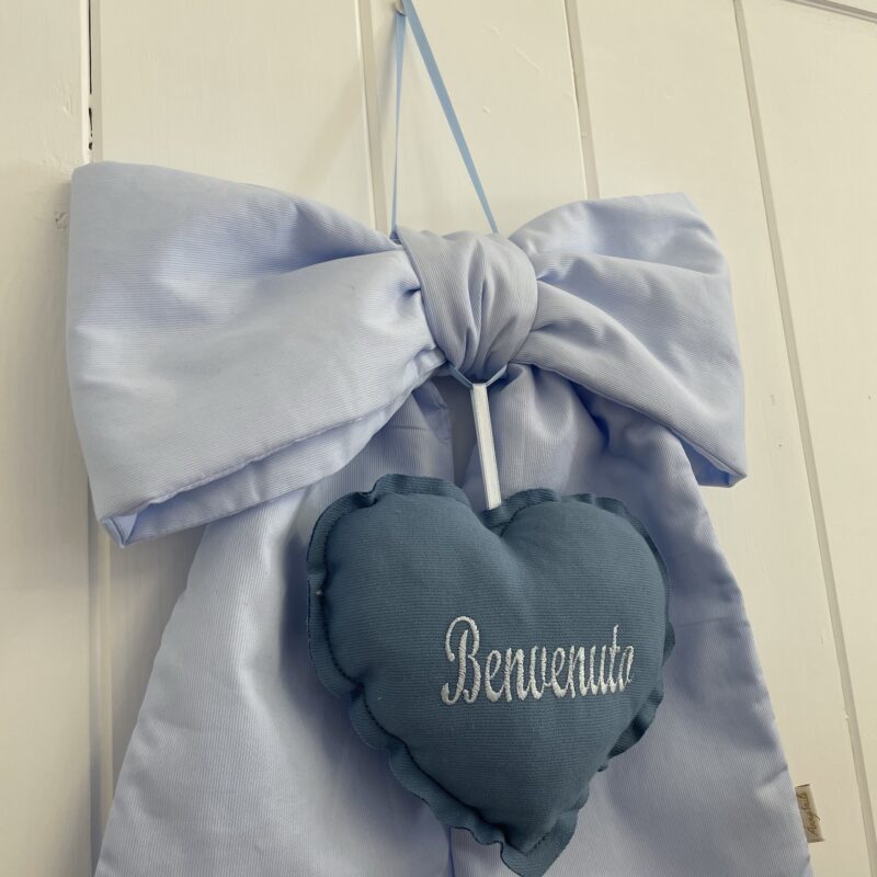 Fiocco con cuore "Benvenuto" sartoriale azzurro in piquet di cotone. Sul cuore blu imbottito in piquet di cotone è ricamata la scritta "Benvenuto".